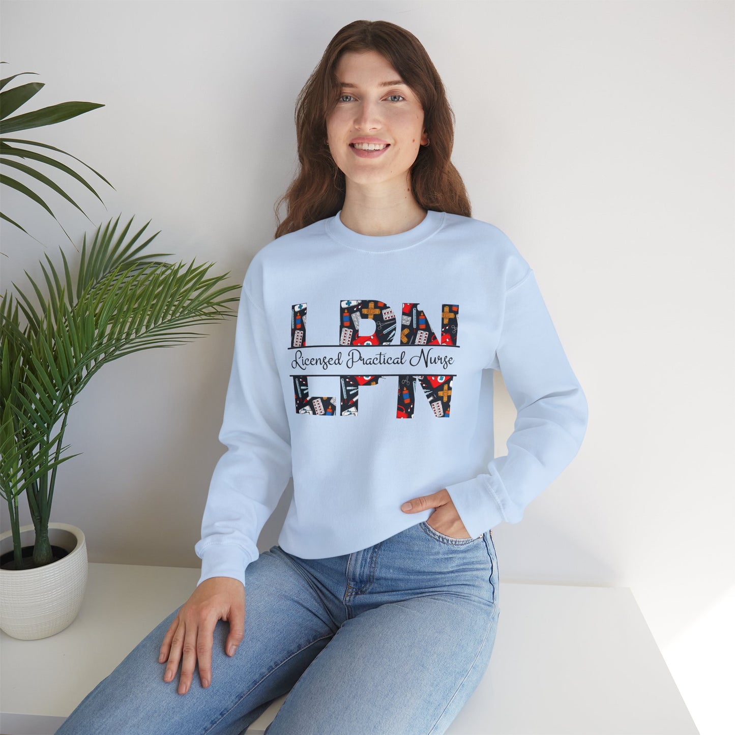 Woman wearing a light blue sweatshirt with 'LPN' and 'Nurse' text, sitting on a white surface with a plant in the background.