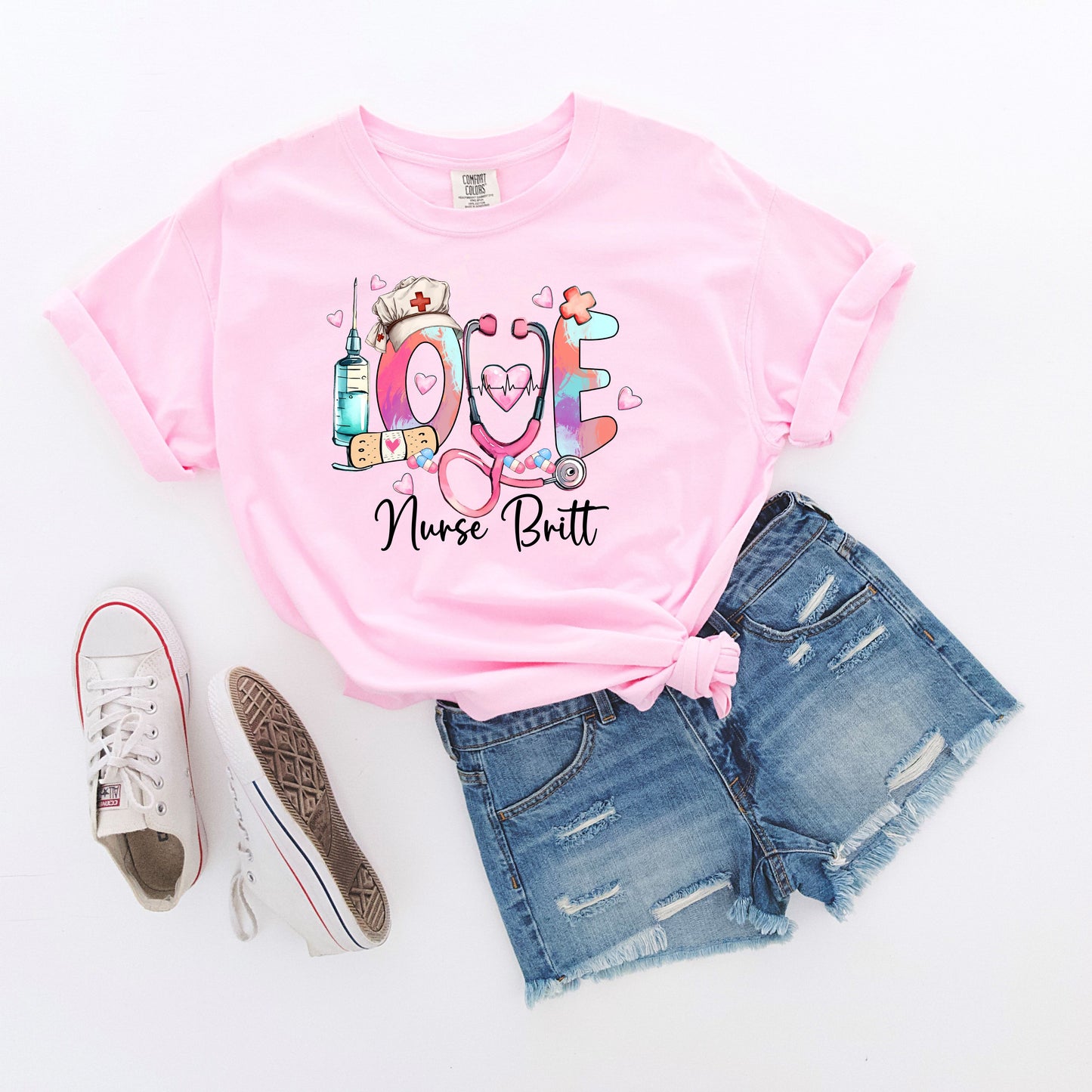 light pink t-shirt with colorful 'LOVE' design featuring a stethoscope, syringe, and nurse's hat on a white background.