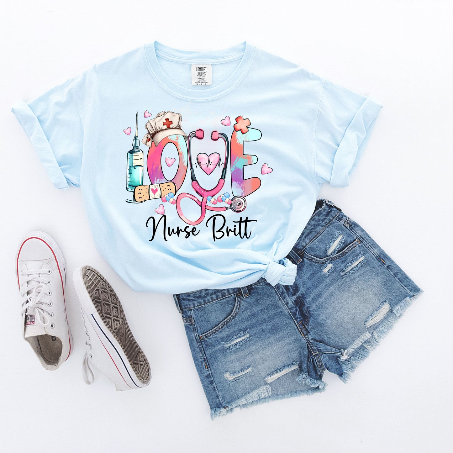 light blue t-shirt with colorful 'LOVE' design featuring a stethoscope, syringe, and nurse's hat on a white background.