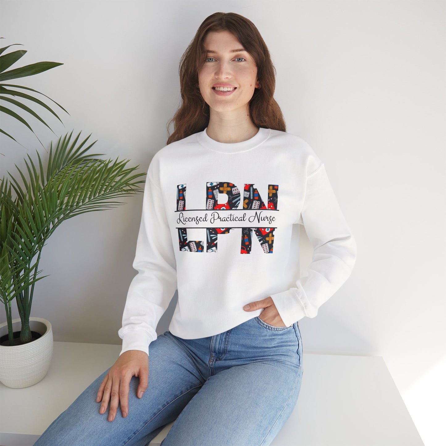 Woman wearing a white sweatshirt with 'LPN' and 'Nurse' text, sitting in a room with a plant.