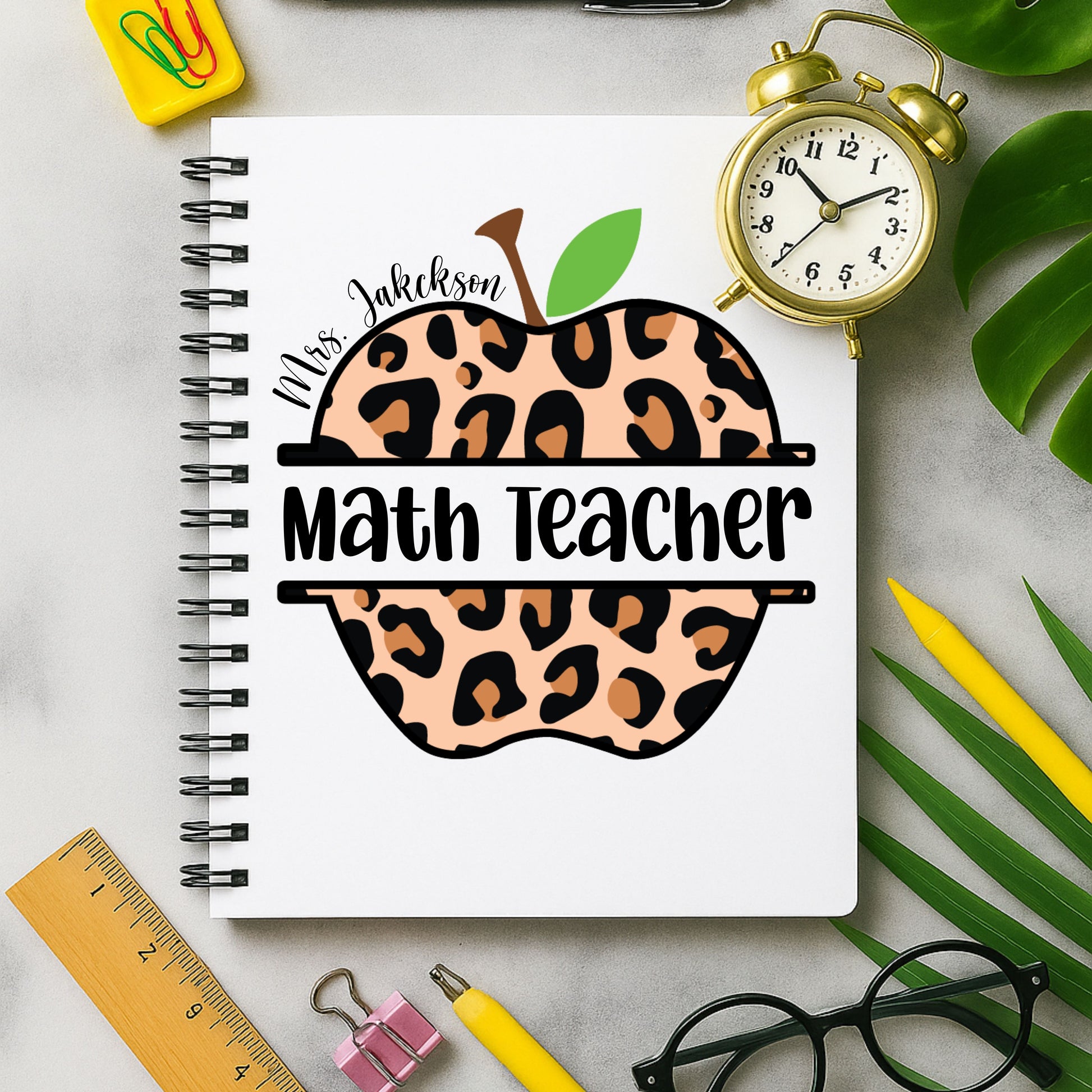 Notebook with leopard print apple design labeled 'Math Teacher' on a desk with stationery items.