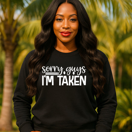 Woman wearing a black sweatshirt with 'sorry guys I'm taken' text in front of palm trees.